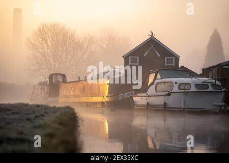 Beautiful foggy misty canal narrow boat sunrise with smoke from chimney early morning with mist and fog rising from water as sun appears along river Stock Photo