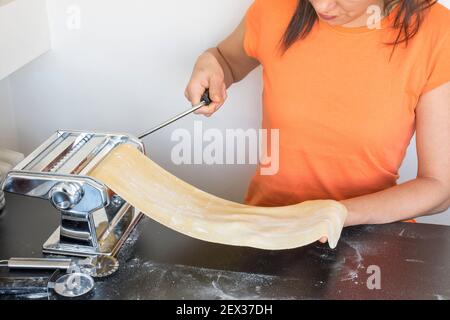 Preparing homemade fettuccine on pasta machine. Cutting raw dough into tagliatelle on special equipment, traditional Italian cuisine concept, copy spa Stock Photo