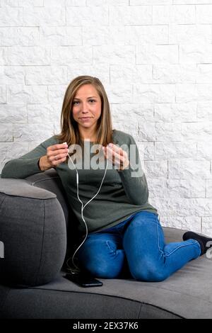 Student sitting on sofa putting on headphones looking smiling into camera Stock Photo