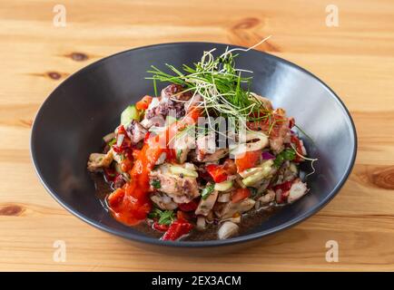Gourmet looking meal of cooked octopus mixed with a vegan salad inside a black bowl. Stock Photo
