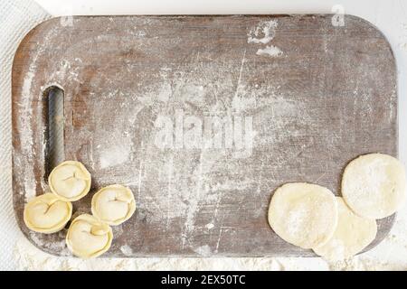 homemade dumplings in the kitchen without decorations. kitchen board sprinkled with flour with dumplings and dumplings dough Stock Photo