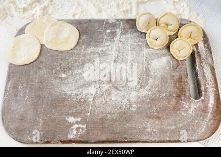 homemade dumplings in the kitchen without decorations. kitchen board sprinkled with flour with dumplings and dumplings dough Stock Photo