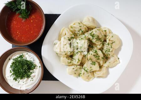 homemade dumplings in the kitchen without decorations. ready-made dumplings on a white plate, served with sour cream and adjika Stock Photo