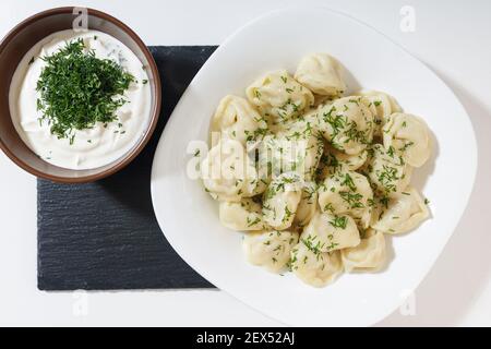 homemade dumplings in the kitchen without decorations. ready-made dumplings on a white plate, served with sour cream Stock Photo