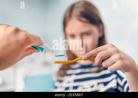dental hygiene. happy little girl brushing her teeth. parents the father squeezes out a colorful toothpaste on the toothbrush in the child's hands. Stock Photo