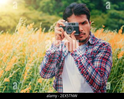 Young hipster man taking photo with old style camera with nature landscape background. Retro and vintage photography concept. Stock Photo
