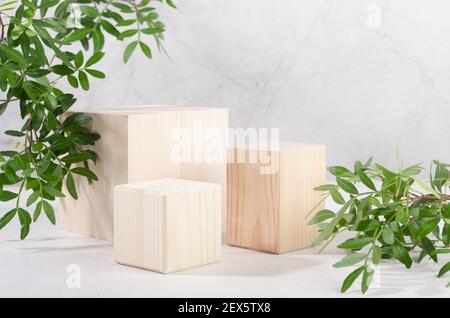 Natural wood cube podiums with green leaves in white, grey marble interior with sunlight, shadow. Showcase for cosmetic products, goods, shoes, bags, Stock Photo