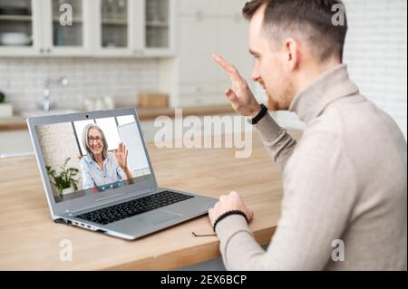 Young handsome hipster man using application for distance video communication with colleague, teacher, tutor, talking with grandmother or boss online, waving at laptop, staying connected in pandemic Stock Photo