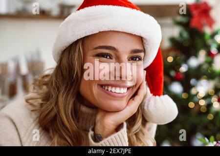 Happy blonde woman in santa claus hat smiling while posing at cozy kitchen Stock Photo