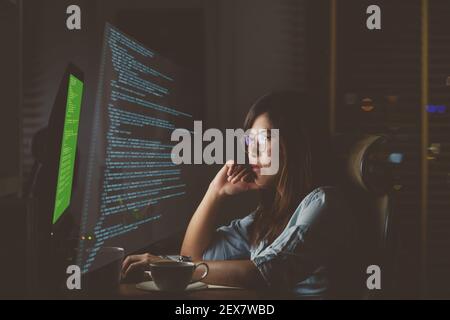 Asian Businesswoman working hard with front of computer desktop with programming source code and motion graphic over computer screen in work place at Stock Photo