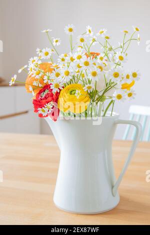 Bouquet of Persian buttercup flowers and daisies in a mint green coffee pot from the 60ies on a wooden table. Scandinavian style interior design. Stock Photo