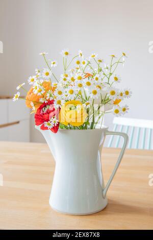 Bouquet of Persian buttercup flowers and daisies in a mint green coffee pot from the 60ies on a wooden table. Scandinavian style interior design. Stock Photo