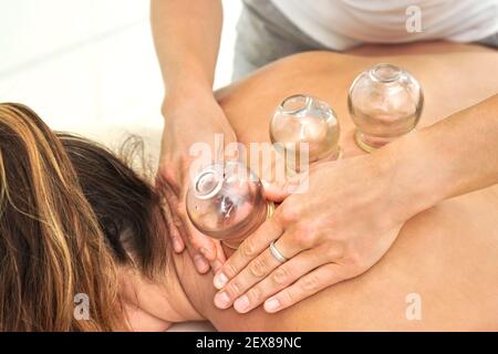 Young female physiotherapist applying glass suction banks on back of her patient, during cupping therapy, closeup detail Stock Photo