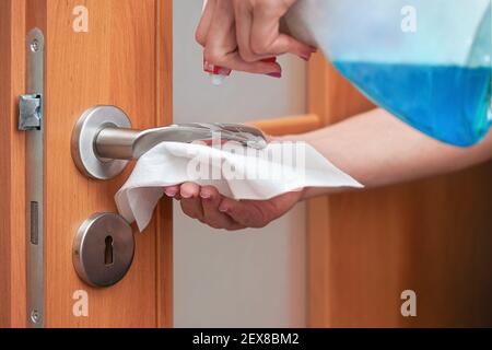 Hand cleaning metal door handle with paper tissue towel, spraying disinfect on it from blue bottle, closeup detail Stock Photo