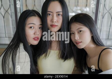 Close up portrait of three beautiful young Asian female friends casually pose for the camera together inside a rustic room in natural light, young chi Stock Photo