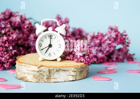 Lilac flowers with vintage tiny alarm clock on blue background. Spring time morning concept. Stock Photo