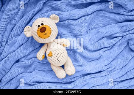 A small knitted amigurumi baby toy-bear is on a blue blanket, flat lay, top view Stock Photo