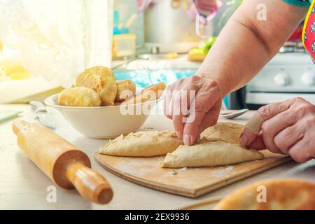 Grandma cooks pies. Home cooked food. omemade cakes of the dough in the women's hands. process of making pie dough by hand Stock Photo