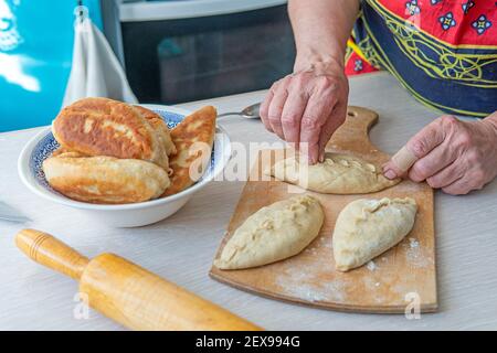 Grandma cooks pies. Home cooked food. omemade cakes of the dough in the women's hands. process of making pie dough by hand Stock Photo