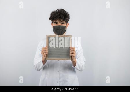 Curly haired young doctor holding board with both hands and directly camera Stock Photo