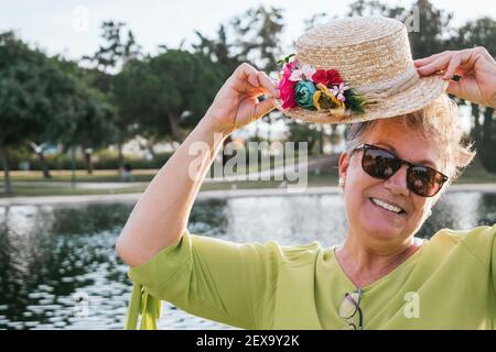 Closeup of a 60 year old woman putting on a hat with in a park Stock Photo