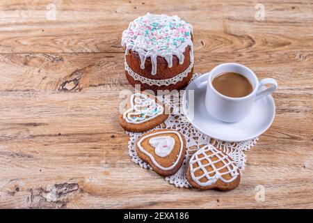 Homemade heart-shaped cookies, decorated with white icing with decorative sprinkles, lie on a crocheted napkin on a wooden table with a cup of coffee, Stock Photo