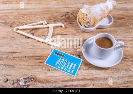 A small coffee cup on a saucer stands on a wooden table next to a notebook and a pen, calculator and caliper, the concept of switching to proper nutri Stock Photo