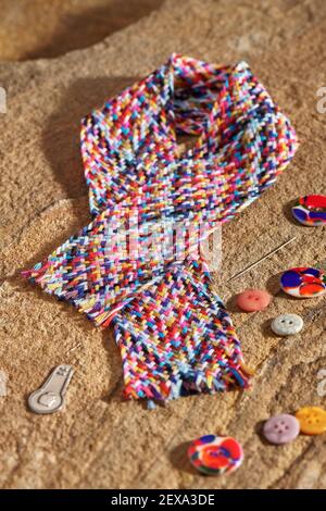 A braid of multi colored sewing threads, needle, needle threader, buttons lying on a stone Stock Photo
