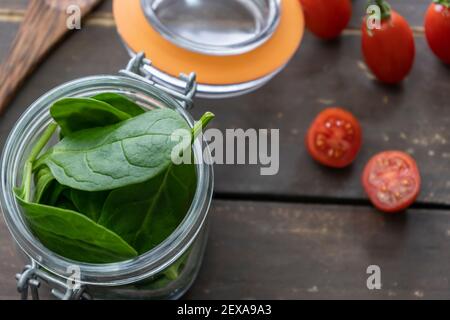 Closeup view of fresh spinach leaves with cherry tomatoes on vintage wooden background.Top view of clean food ingredients,bio organic vegan concept. Stock Photo