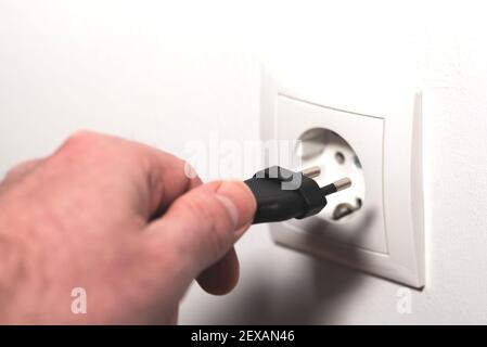 close-up of hand inserting power cord plug into wall outlet or pulling plug from socket Stock Photo