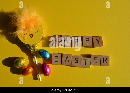 Happy Easter in wooden alphabet letters with foil wrapped chocolate eggs and chick lollipop Stock Photo