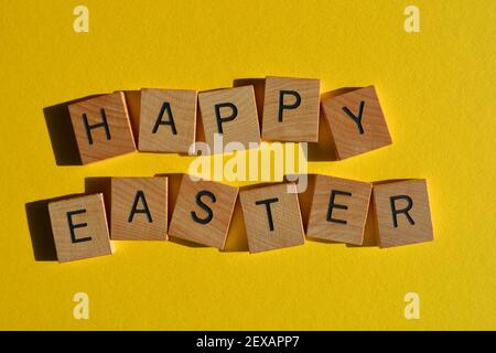 Happy Easter, words in wooden alphabet letters isolated on bright yellow background Stock Photo