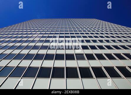Low angle view on skyscraper facade with geometric symmetrical pattern lines against deep blue cloudless sky Stock Photo
