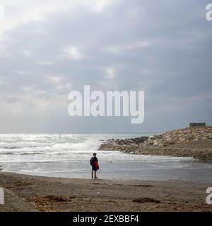 Young man walking alone at the mouth of the Guadalhorce river in Malaga on a cloudy winter day. Stock Photo