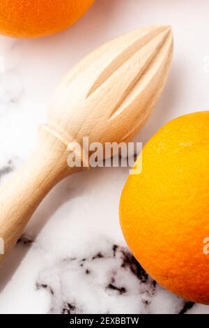 Top view of wooden juicer and two oranges on white marble, vertical Stock Photo