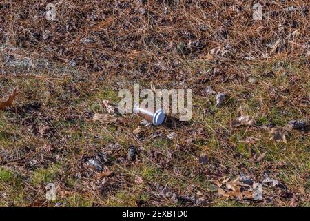 A paper takeout cup of coffee with plastic lid discarded on the ground carelessly in the park polluting the environment Stock Photo