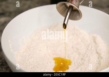 Pouring olive oil on flour for a bread dough. Preparing bread at home. Stock Photo