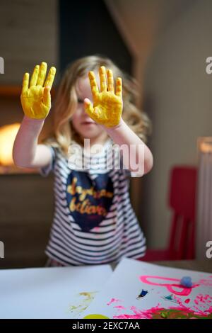 Cute little artist girl showing yellow painted palms to the camera with mother a side. Stock Photo