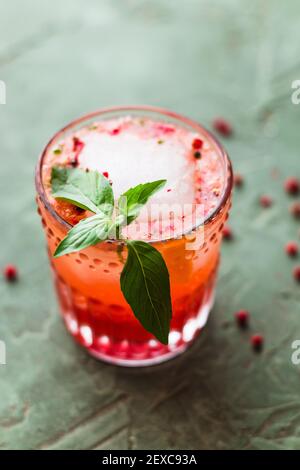 Red and pink drink garnished with an ice cube and basil Stock Photo