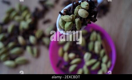 Female is putting green cardamom pods in a spoon. Dry cloves, cardamoms and spicy spices background. Veg Recipes Stock Photo