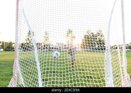 A soccer ball in mid-air after a young boy kicks the ball into the net Stock Photo