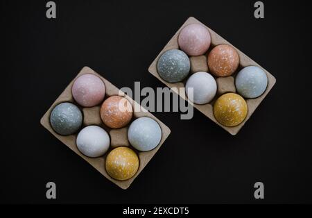 Overhead view of colorful Easter eggs in egg carton on black Stock Photo