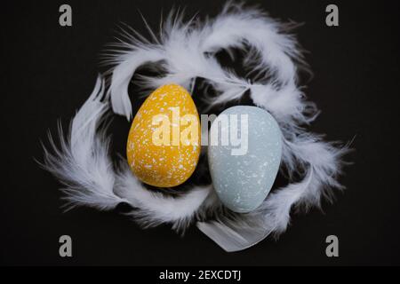 Overhead view of colored Easter eggs and feathers on black background Stock Photo