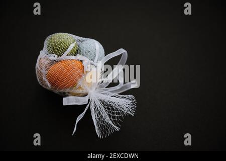 Colored Decorative Easter eggs in white mesh bag on black background Stock Photo