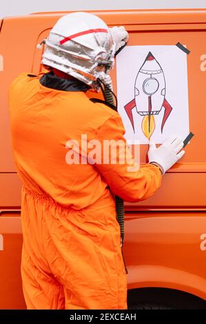 Man disguised as an astronaut sticks a poster with a drawing of a rocket on the van Stock Photo