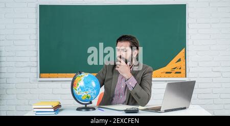 mature bearded man teacher in costume sit in school classroom with geography globe map, location. Stock Photo