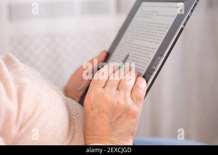 Old woman using eBook relaxing on sofa, old woman's hands hold a ebook, close up Stock Photo