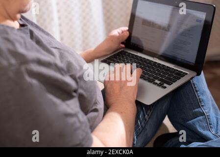 Old woman using a laptop, surfing the internet, hands holding a computer, working from home office, close up. Stock Photo