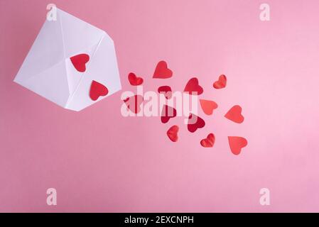 Red hearts flying out of a white envelope on a pink background, close up. Valentine's Day card. Stock Photo