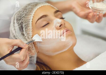Beautician applies white cosmetic cream to a girl lying on a massage table. Close up. Stock Photo